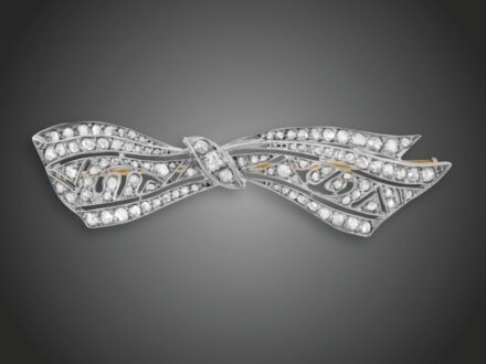155. tétel, Melltű  Arany és ezüst, szalagcsokorforma, áttört mintán 3 régi csiszolású briliáns cca. 0,15 ct (R2CrSi) és apró rózsacsiszolású gyémántok cca. 1,0 ct ékítéssel, 1920 körül, 6,2 g
