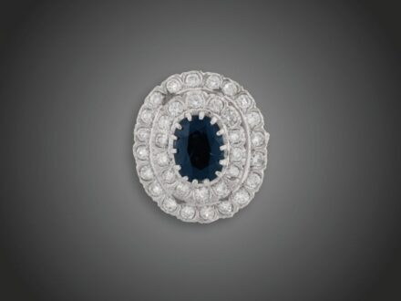 123. tétel, Női gyűrű  Fehérarany 585, ovális formájú, karmos foglalású kék zafír cca. 2,50 ct, körülötte 2 sorban foglalt 34 briliáns cca. 1,30 ct (MTCrSi) karmazált fazonban, 8,9 g, átmérő: 17,8 mm, 1 kő törött