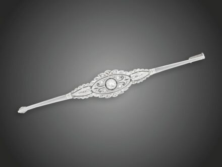 1. tétel, Melltű  Fehérarany 750, egyenes pálcán áttört díszítő elem, 1 briliáns cca. 0,15 ct (R1CrSi) és 12 apró gyémánt cca. 0,05 ct ékítéssel, 1930 körül, 5,2 g