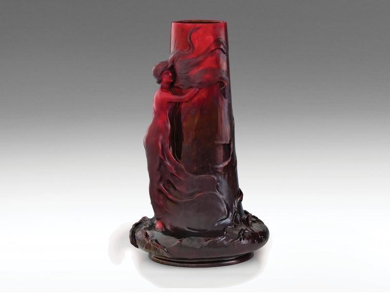 471. tétel, Zsolnay váza nőalakkal  Fehércserép, formába öntött. Felületén színes eozinmázakkal festett fényes és matt felületek, részben savmaratott. Talpán felül restaurált.  Formaterv: Mack Lajos, 1900.  Forma: 9. Facon-könyv, 5955. sz. rajz, „Mack Laj