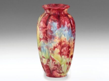 469. tétel, Zsolnay szecessziós díszváza  Formába öntött porcelánfajansz. Gerezdelt palástján színes majolikamázakkal festett virágos díszítmény.   Alján jelzett: masszába nyomott 5452 (1899. évi formaszám) és kerek, kidomborodó, pecsétszerű márkajelzés.