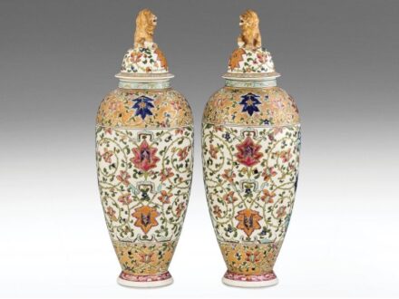 445. tétel, Fischer fedeles váza-pár  Formába öntött porcelánfajansz, peremein aranybrokát díszítménnyel. Felületén kidomborodó, színes zománccal festett keleties virágdekor, fedelein plasztikus oroszlán díszek. Szájperemeken hajszálrepedt, egyik fedélen