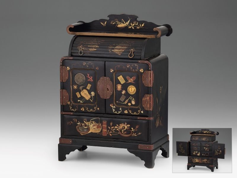 399. tétel, Japán ékszertartó szekrényke Fekete lakkfa, felületén vörös és aranyfestéssel, ill. ajtajaiba beágyazott japán érmékkel és plakettekkel. Felső párkányán ragasztás. Eredeti kulccsal. Japán, XX. eleje. M.: 25 × 14,8 × 34 cm