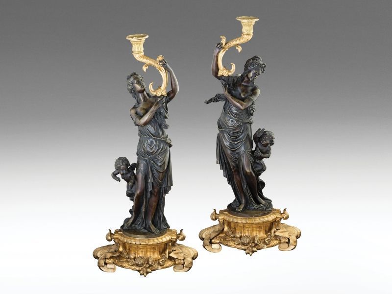 398. tétel, Figurális kandeláber-pár Öntött, patinázott részben tűzaranyozott bronz. Barokk stílusú girlandos talapzatán allegorikus nőalakok, kezükben akantuszos gyertyatartóval. Oldalain galambot tartó, illetve nyilazó puttókkal. Az egyik alak karj