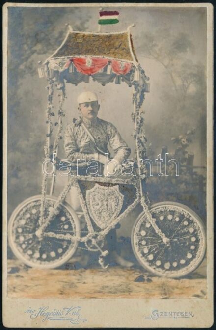 cca 1910 Virágokkal feldíszített kerákpáros fotója, kézzel színezett keményhátú fotó Hegedűs vilmosné szentesi műterméből, szecessziós hátlappal, 16,5×10,5 cm / bicyclist, coloured vintage photo