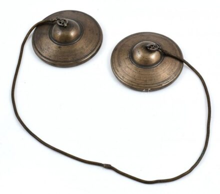 Tibeti szertartási cintányér (Tingsha), fém láncon, d: 7,8 cm, h. 55 cm. 'Két kisméretű, ám vastag öntött kis cintányér bőrszíjjal összekötve. A cintányérok anyaga bronz vagy 7 fém. Összeütve őket csodásan egyedülálló, a