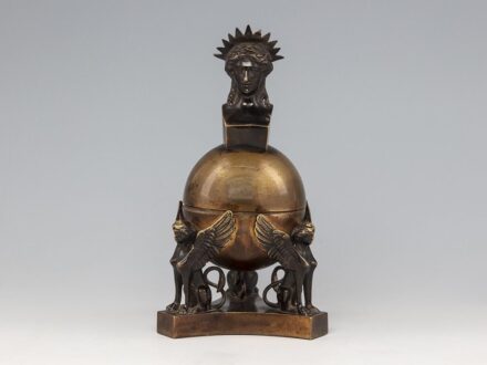 Historizáló tintatartó_x000D_
Öntött, patinázott bronz. Három szphinx tartja a földgömb formájú tintatartót._x000D_
Zsanéros nyitódású fedelén Aurora a hajnal istennőjének mellszobra található. Üvegbetétje hiányzik._x000D_
1920 körül._x000D_
M.: 21,5 cm