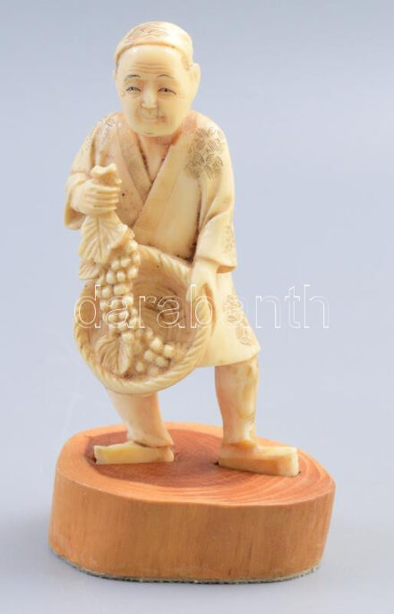 Japán okimono. Szőlőfürtöt tartó férfi. Faragott csont, XX. sz eleje. 11 cm hozzá fa tartó.        Japanese okimono. Man holding a bunch of grapes. Carved bone, early 20th century. 11 cm wooden stand included.