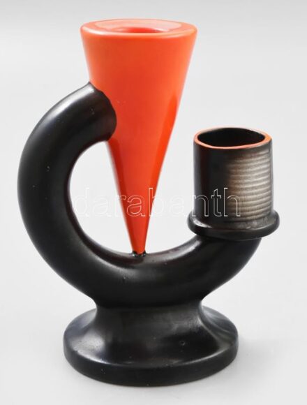 Goebel art deco gyertyatartó. Klasszikus art deco geometrikus formavilág: fordított kúpot körülölelő hajlított csőalak, fekete és narancssárga mázakkal festve, szélső elemen recézett gyufagyújtó felülettel. Alján kereskedői címke: "Hay Miksa Szeged 1897".