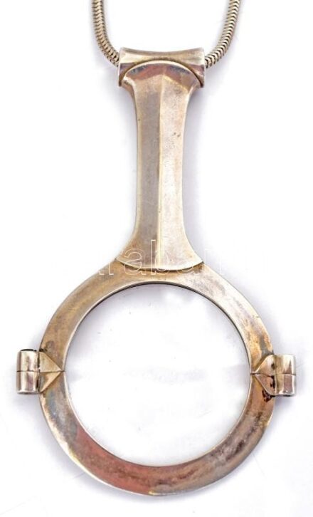 Ezüst(Ag) Péter Vladimir (1947-) által tervezett nagyító láncon, jelzett (Wladis), h: 76 cm, bruttó: 52,1 g, reprodukálva a Horváth-Kelényi-Buzinkay-Ébli: Értékmentő szenvedély című könyv 97. oldalán. Kiállítva: Bp., 2008, Iparművészeti